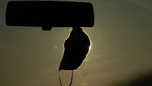 Eine FFP2-Maske hängt vor der aufgehenden Sonne in einem Auto