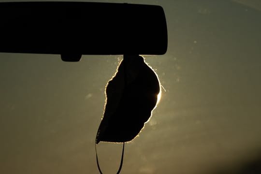 Eine FFP2-Maske hängt vor der aufgehenden Sonne in einem Auto
