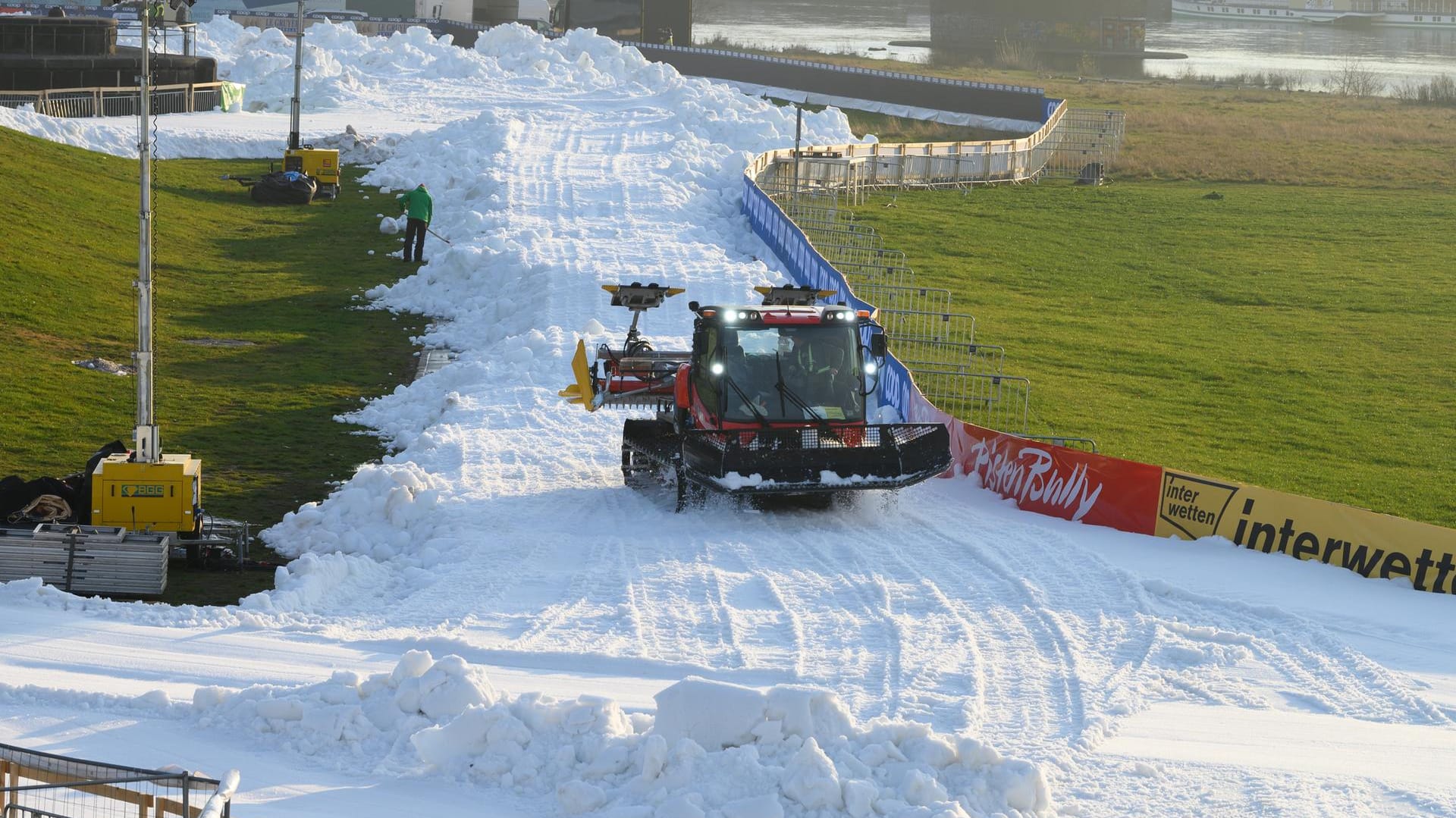 Ein Pistenbully präpariert am Elbufer eine künftige Wettkampfstrecke mit Kunstschnee: Trotz des Lockdowns wird der Skilanglauf-Weltcup in Dresden durchgeführt.