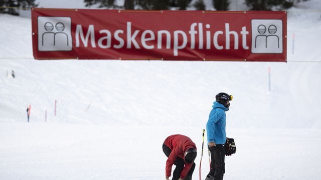 Zwei Skifahrer stehen unter einem Banner im Skigebiet Flumserberg, das auf die Maskenpflicht hinweist. Zwei Skifahrer stehen unter einem Banner im Skigebiet Flumserberg, das auf die Maskenpflicht hinweist.