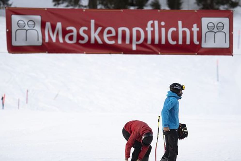 Zwei Skifahrer stehen unter einem Banner im Skigebiet Flumserberg, das auf die Maskenpflicht hinweist.
