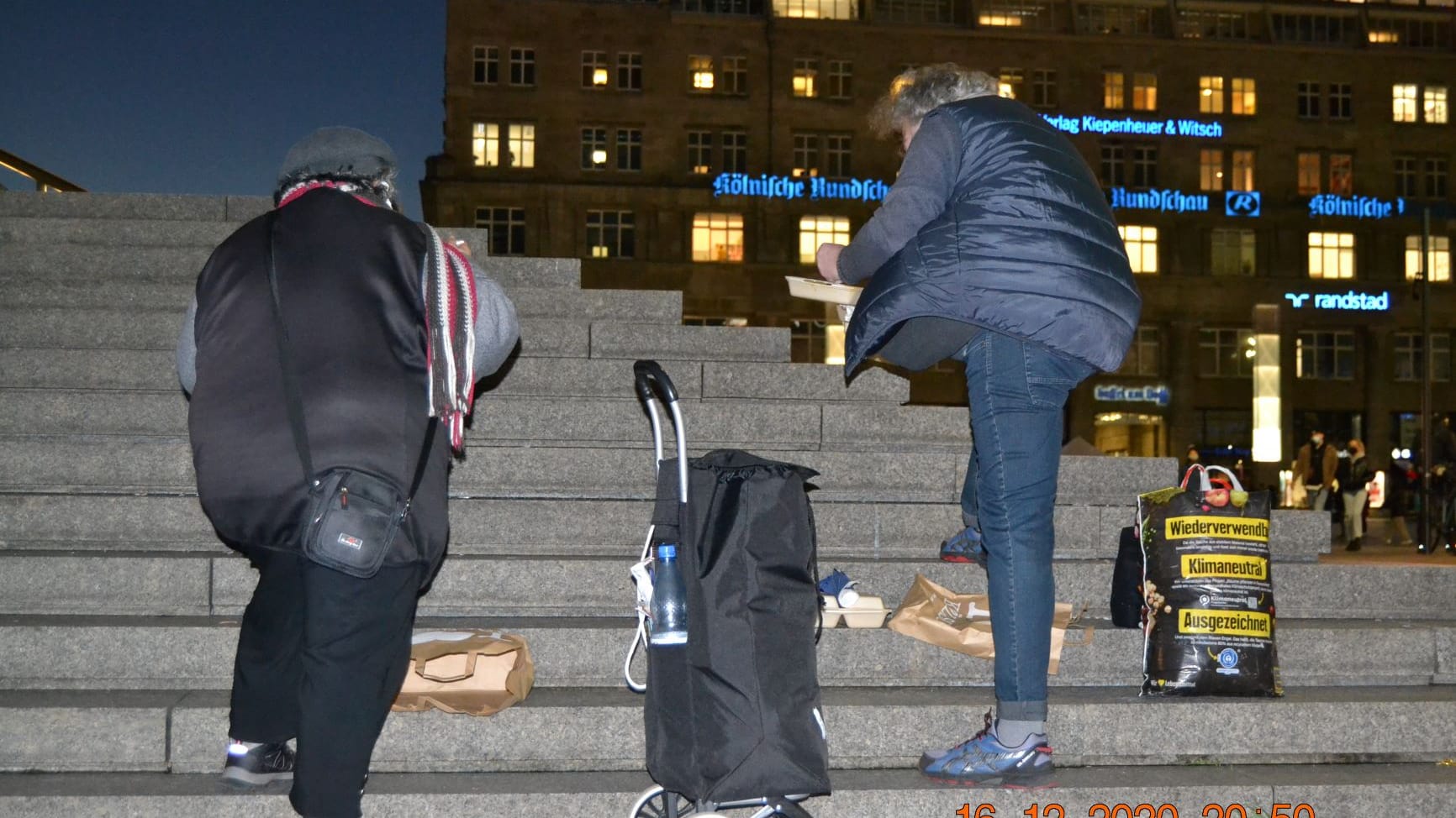 Zwei Personen stehen auf der Domtreppe und essen. Wegen der Pandemie können sich wohnungslose Personen nicht mehr im Hauptbahnhof aufwärmen.