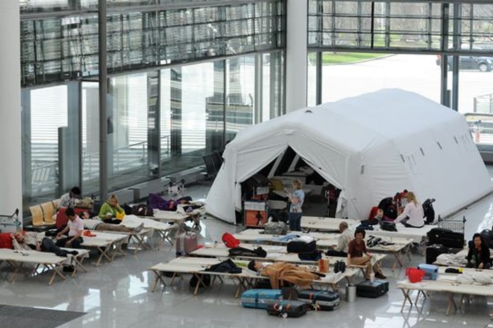 Fluggäste sitzen am Münchener Flughafen auf Feldbetten in einer Notunterkunft im Terminal 2.