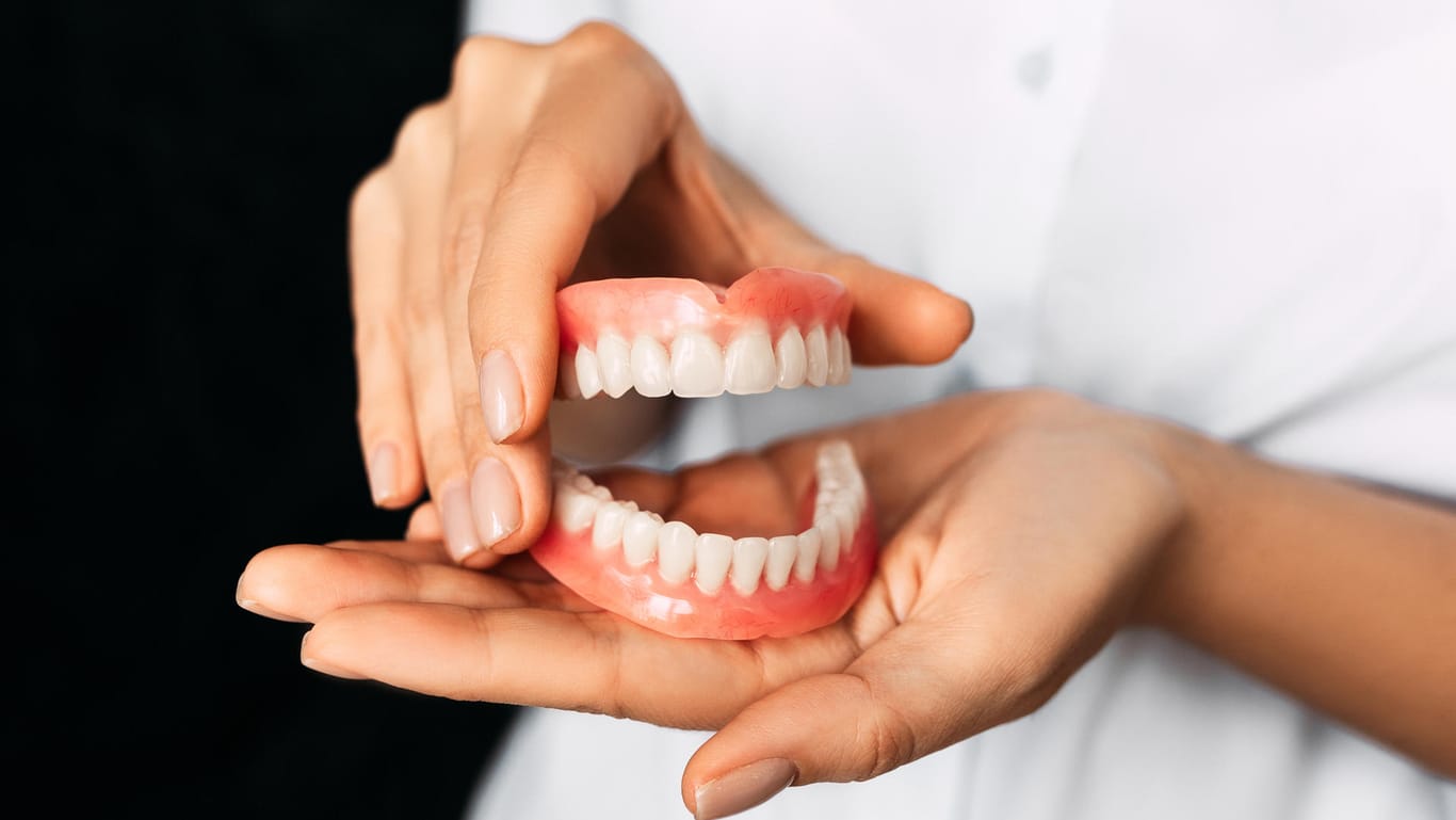 Eine Zahnärztin hält eine Zahnprothese in der Hand: Auch wenn es sich um "die Dritten" handelt, brauchen sie ebenso gute Pflege wie echte Zähne.