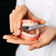 Eine Zahnärztin hält eine Zahnprothese in der Hand: Auch wenn es sich um "die Dritten" handelt, brauchen sie ebenso gute Pflege wie echte Zähne.