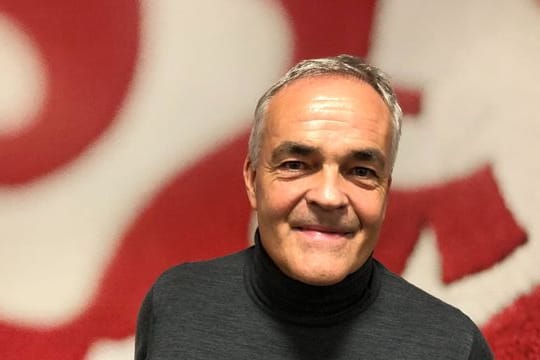 Der Vorsitzende des Vereinsbeirats des VfB Stuttgart, Wolf-Dietrich Erhard, steht vor einem großen Vereinswappen.