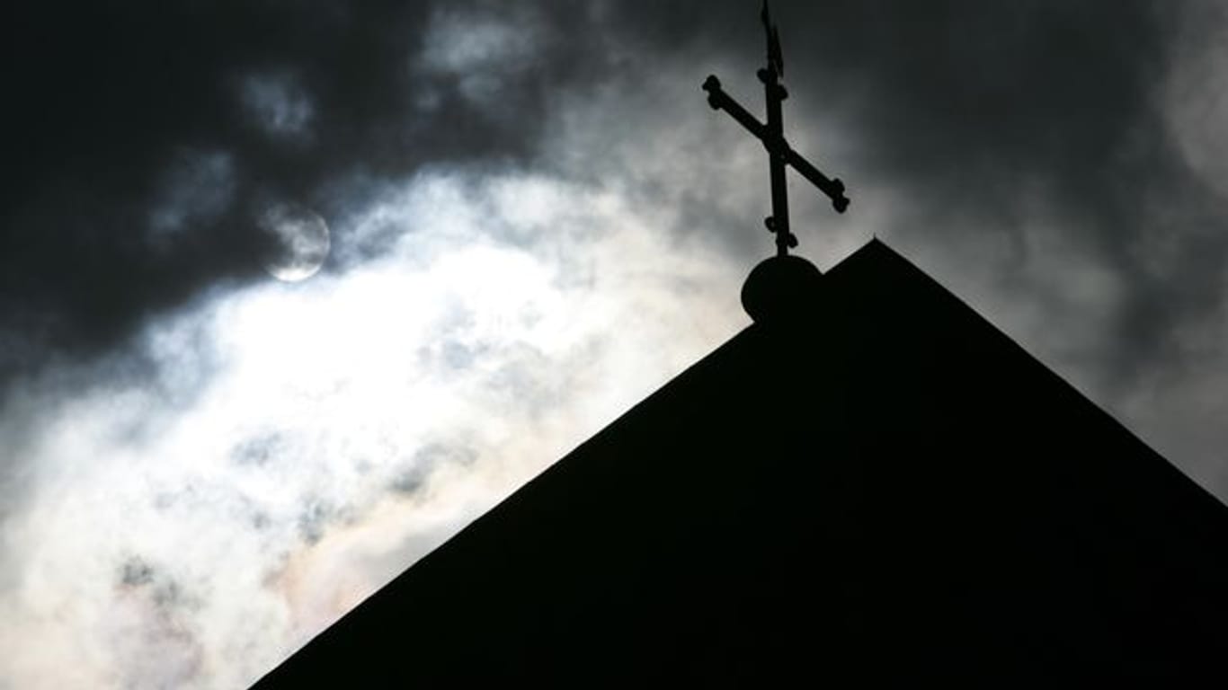 Eine Kirchturmspitze eines Doms mit Kreuz vor wolkenverhangenem Himmel.