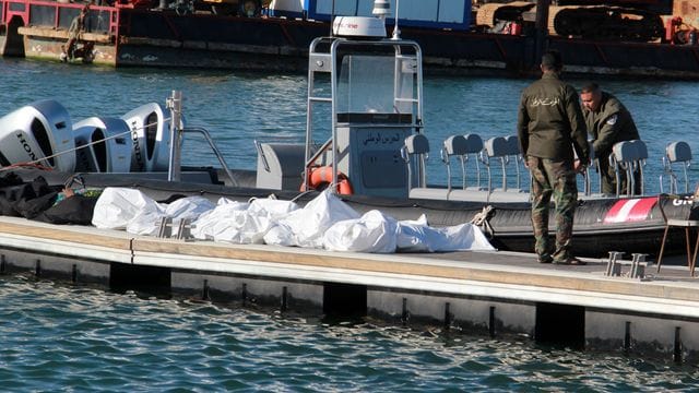 Einsatzkräfte der tunesischen Küstenwache im Hafen von Sfax neben zugedeckten Leichen auf einem Steg. Einsatzkräfte der tunesischen Küstenwache im Hafen von Sfax neben zugedeckten Leichen auf einem Steg.