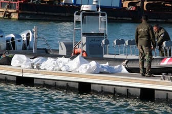 Einsatzkräfte der tunesischen Küstenwache im Hafen von Sfax neben zugedeckten Leichen auf einem Steg.