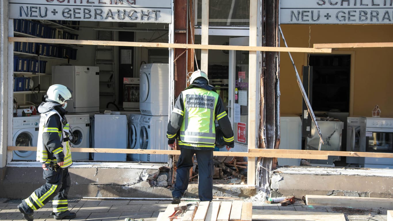 Feuerwehrleute stehen vor einem zerstörten Ladenlokal: In dieses Geschäft soll ein 16-Jähriger in Wuppertal gekracht sein, nun ist das Haus einsturzgefährdet.
