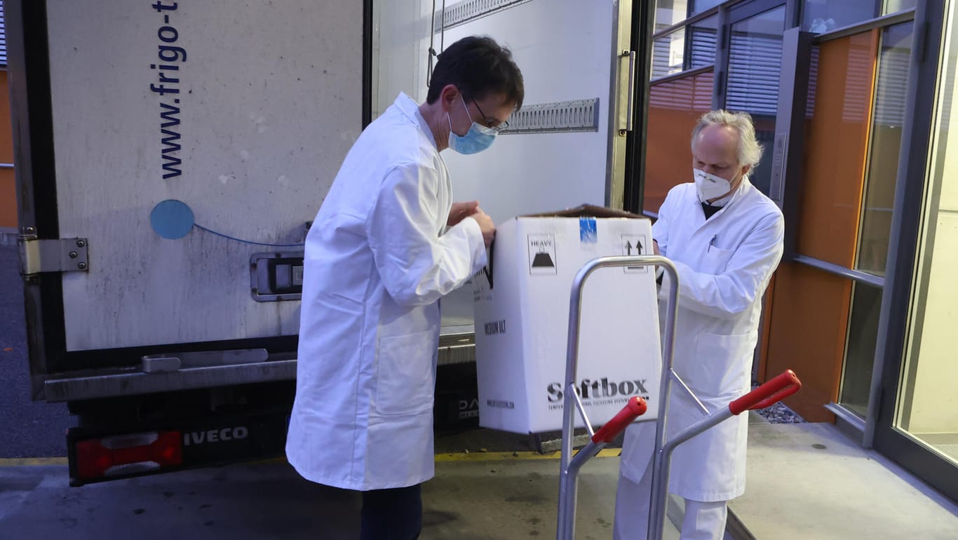 Mitarbeiter transportieren einen Karton mit einigen der ersten knapp 10.000 Dosen Corona-Impfstoff für Thüringen in ein Gebäude.