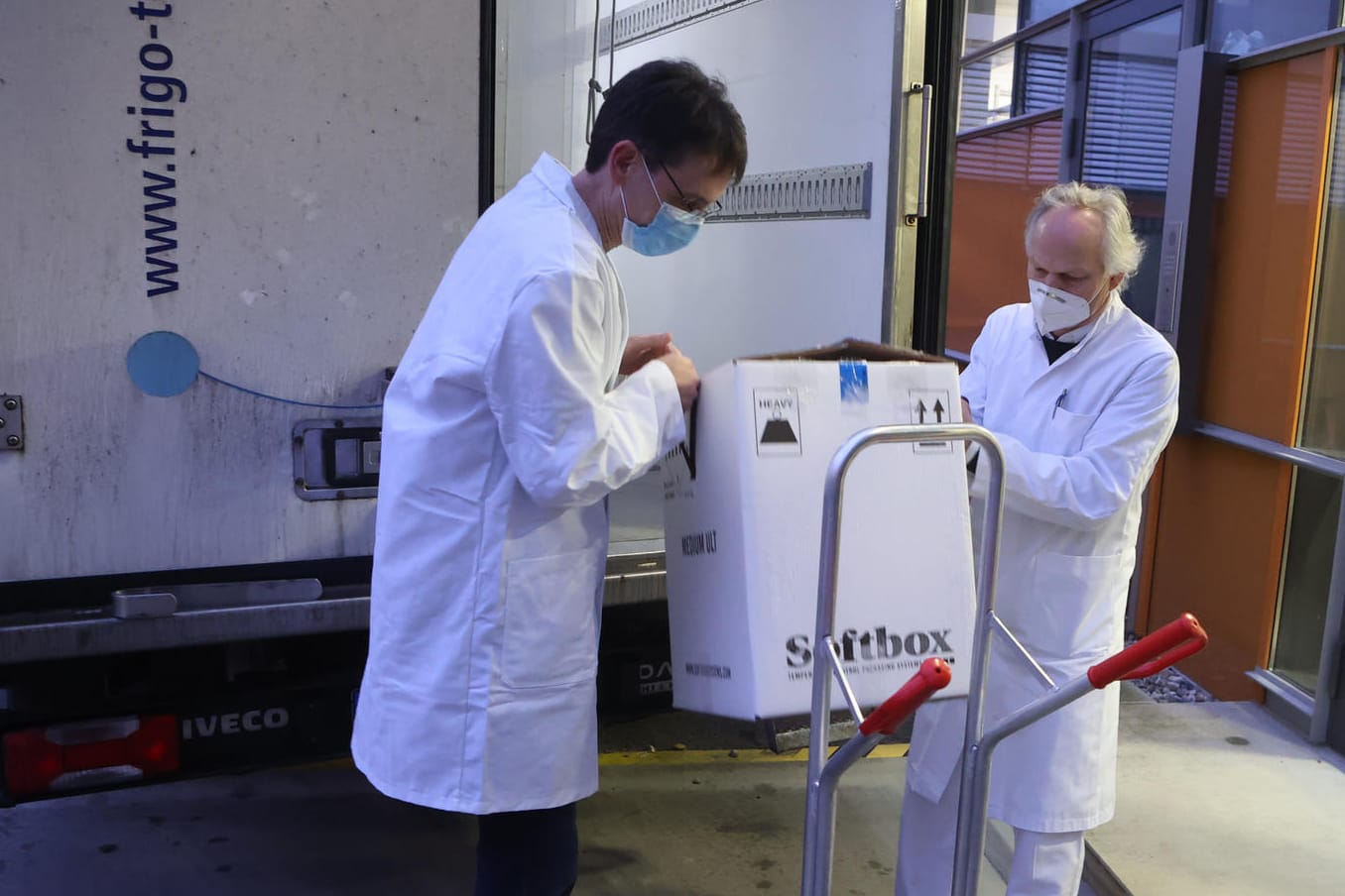 Mitarbeiter transportieren einen Karton mit einigen der ersten knapp 10.000 Dosen Corona-Impfstoff für Thüringen in ein Gebäude.