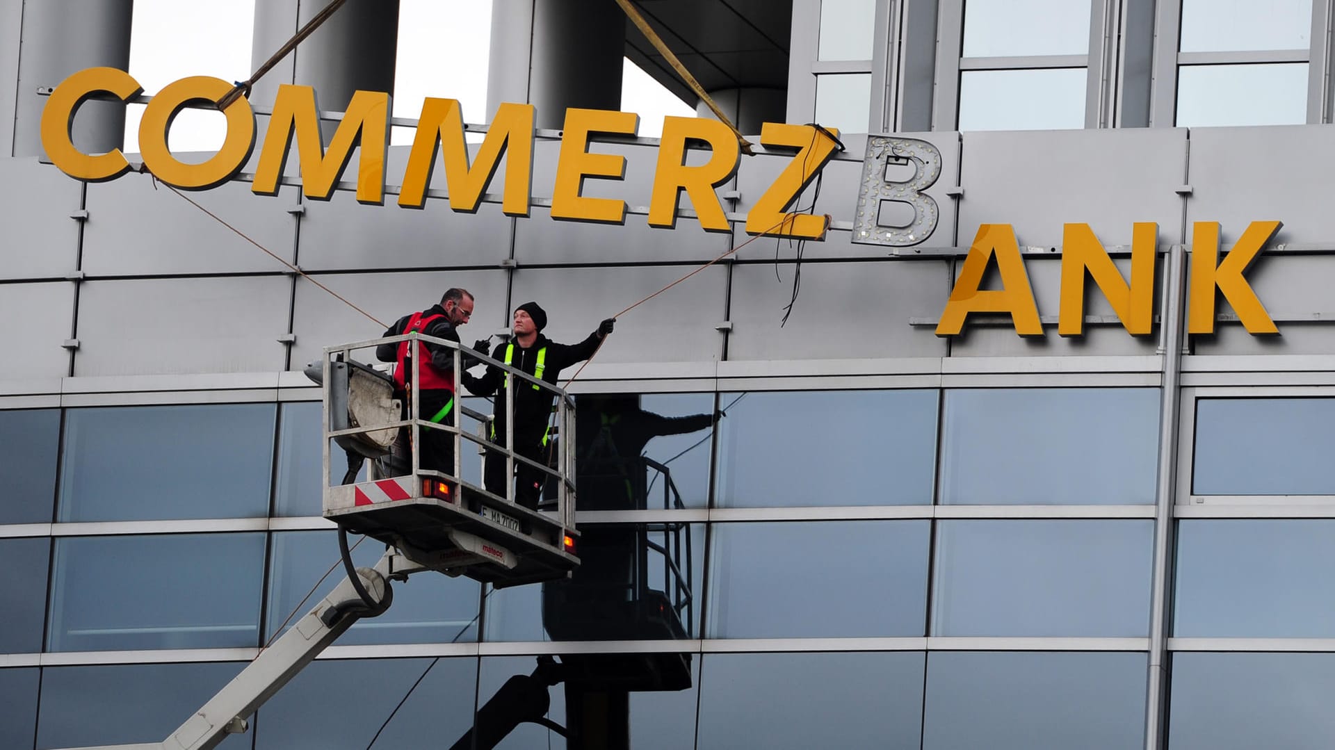 Arbeiter demontieren den Schriftzug einer Commerzbank-Filiale: Die Bank baut drastisch um.