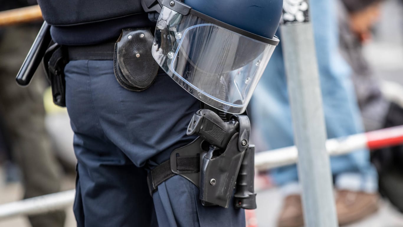 Ein Polizist trägt einen Schutzhelm und einen Schlagstock am Körper (Symbolbild): Bei Ermittlungen gegen einen Polizisten soll geklärt werden, ob er das Beherbergungsverbot umgehen wollte.