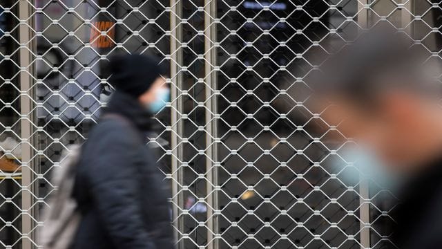 Menschen mit Mundschutz gehen an einem geschlossenen Geschäft in der Königsstraße in Stuttgart vorbei.