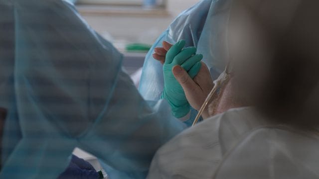 Eine Ärztin hält in einer Intensivstation die Hand eines Coronapatienten.
