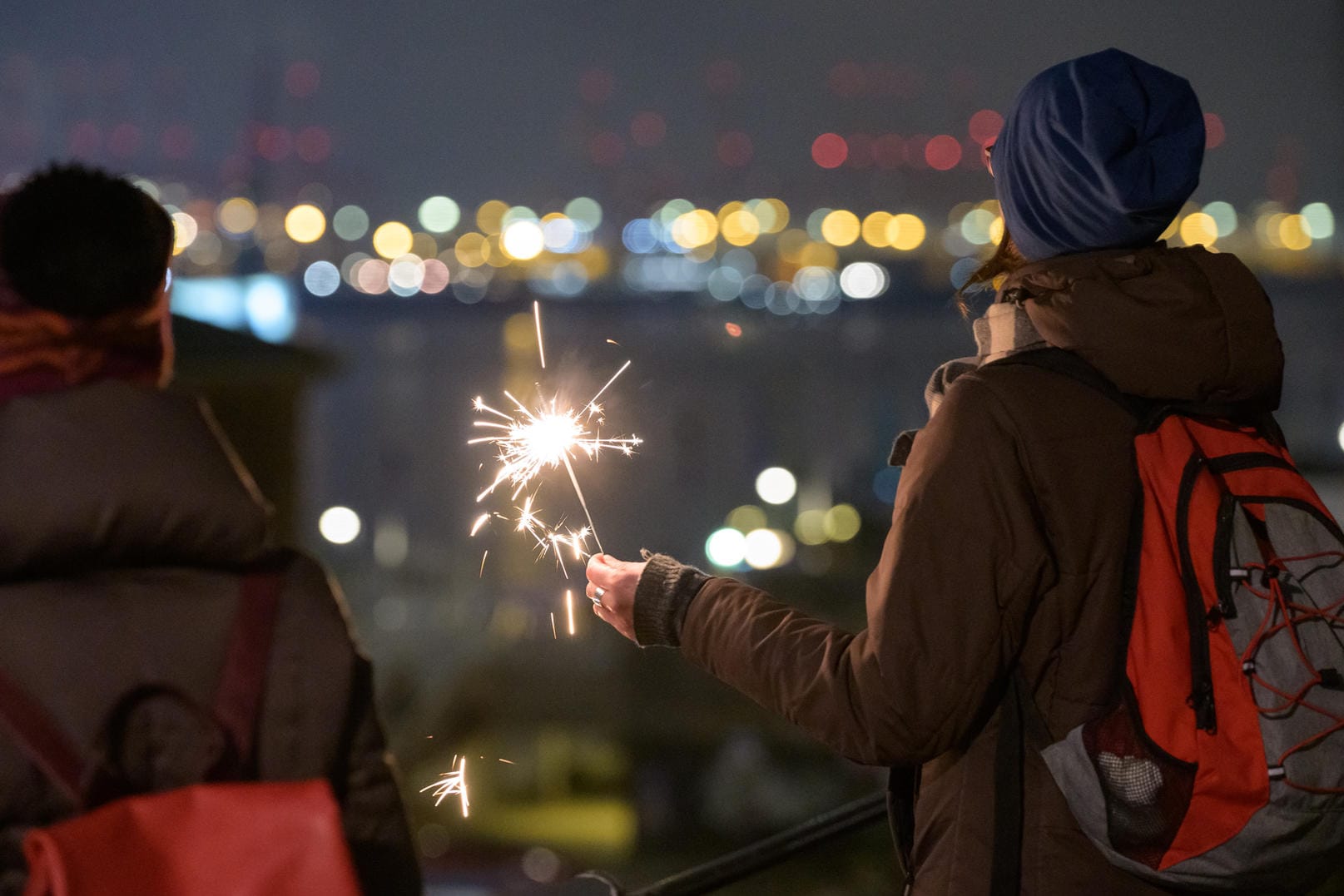 Silvester 2020/2021: Eine Frau hat kurz nach dem Jahreswechsel eine Wunderkerze gezündet und schaut auf das Hafenpanorama.