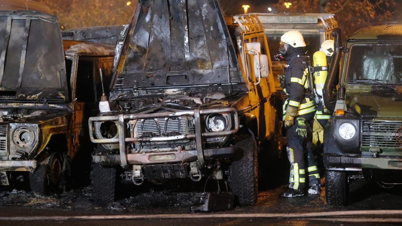 Ein Feuerwehrmann steht an abgebrannten Geländewagen: Auf dem Gelände eines Autohandels wurden Fahrzeuge angezündet.