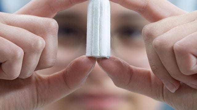 Ein Tampon wird von einer Angestellten in einer Produktionshalle gehalten. Ein Tampon wird von einer Angestellten in einer Produktionshalle gehalten.