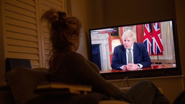 Eine Frau verfolgt im Fernsehen die Ansprache von Premierminister Boris Johnson an die Nation. Eine Frau verfolgt im Fernsehen die Ansprache von Premierminister Boris Johnson an die Nation.
