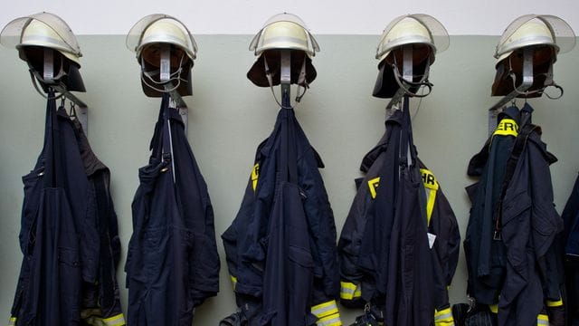 Feuerwehruniformen hängen aufgereiht an einer Wand Feuerwehruniformen hängen aufgereiht an einer Wand