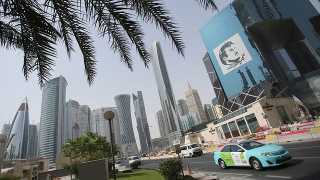 Ein Taxi fährt in Doha an einem Gebäude mit einem Bild des Emirs von Katar, Tamim bin Hamad Al Thani, vorbei.