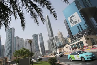 Ein Taxi fährt in Doha an einem Gebäude mit einem Bild des Emirs von Katar, Tamim bin Hamad Al Thani, vorbei.