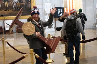 Einer der Eindringlinge ins Kapitol von Washington trägt ein Rednerpult weg: Bei der Besetzung des US-Parlamentsgebäudes fanden offenbar auch Plünderungen statt.