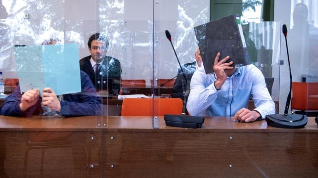 Die beiden angeklagten Männer verdecken vor Prozessbeginn ihre Gesichter. Die beiden angeklagten Männer verdecken vor Prozessbeginn ihre Gesichter.