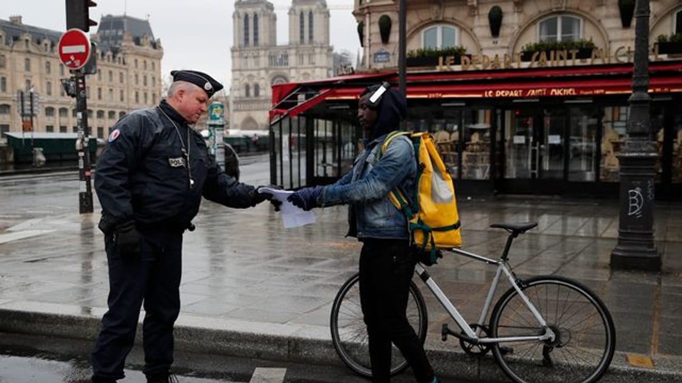 Ein französischer Polizeibeamter überprüft in Paris die Genehmigung eines Passanten, sich weiter als einen Kilometer vom Wohnort zu entfernen.