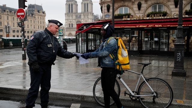 Ein französischer Polizeibeamter überprüft in Paris die Genehmigung eines Passanten, sich weiter als einen Kilometer vom Wohnort zu entfernen. Ein französischer Polizeibeamter überprüft in Paris die Genehmigung eines Passanten, sich weiter als einen Kilometer vom Wohnort zu entfernen.