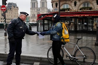 Ein französischer Polizeibeamter überprüft in Paris die Genehmigung eines Passanten, sich weiter als einen Kilometer vom Wohnort zu entfernen.
