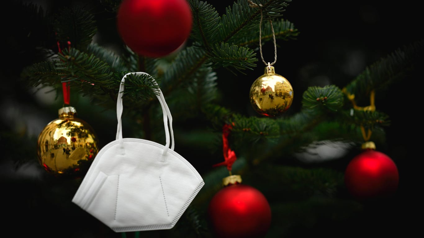 Eine FFP2-Maske hängt in einem Weihnachtsbaum (Symbolbild): Der Großteil der in Erfurt am Donnerstag gemeldeten Corona-Neuinfektionen ist auf private Weihnachtsfeiern zurückzuführen.