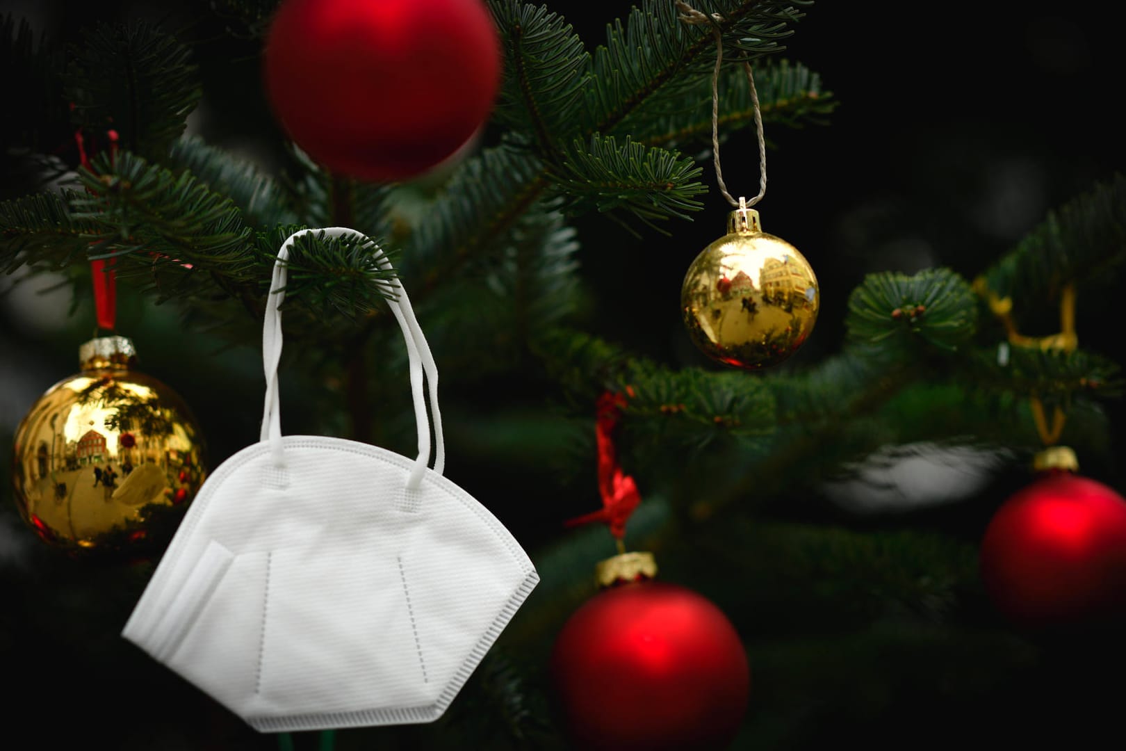 Eine FFP2-Maske hängt in einem Weihnachtsbaum (Symbolbild): Der Großteil der in Erfurt am Donnerstag gemeldeten Corona-Neuinfektionen ist auf private Weihnachtsfeiern zurückzuführen.