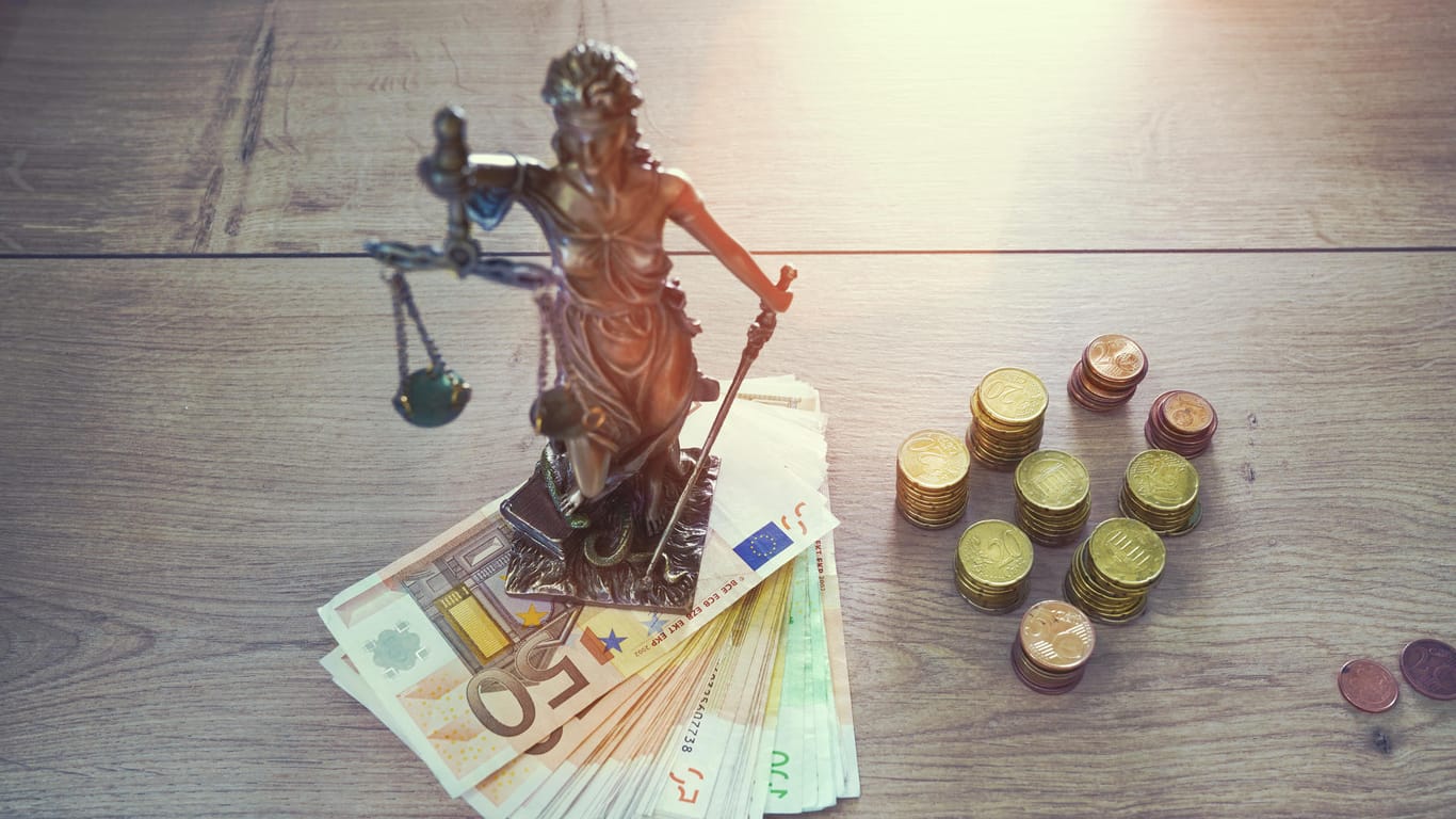 Statue der Justitia mit Münzen und Scheinen (Symbolbild): Kriminelle sollen die Corona-Krise ausnutzen, um an Geld zu kommen.