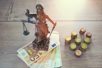 Statue der Justitia mit Münzen und Scheinen (Symbolbild): Kriminelle sollen die Corona-Krise ausnutzen, um an Geld zu kommen.