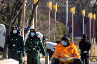 Chinesische paramilitärische Polizisten mit Mund-Nasen-Schutz patrouillieren entlang einer Straße in Peking.
