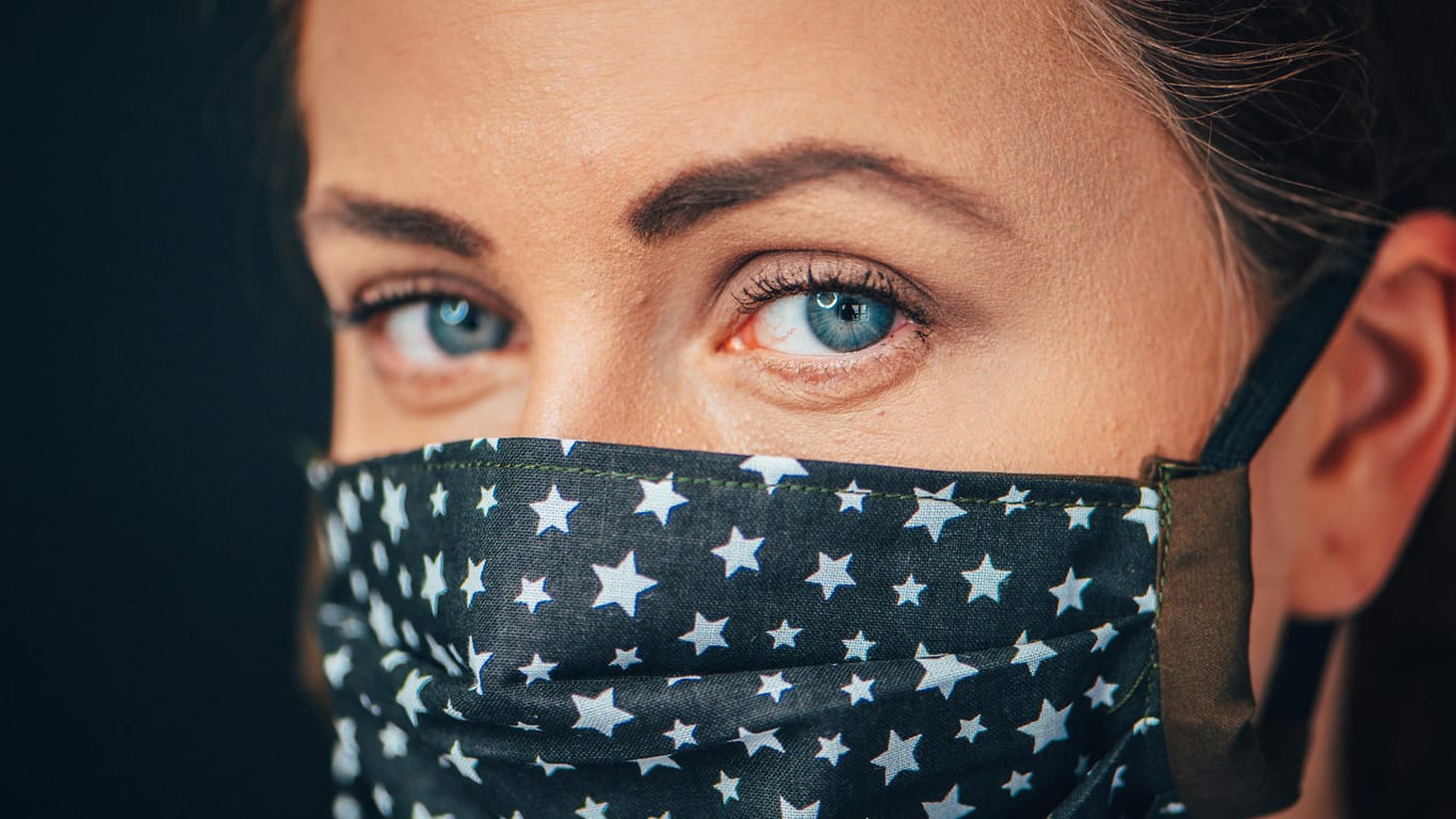 Eine Frau mit leicht geröteten Augen trägt eine Alltagsmaske: Sitzt diese an der Nase nicht richtig, strömt Luft zu den Augen und lässt sie austrocknen.