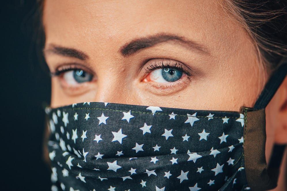 Eine Frau mit leicht geröteten Augen trägt eine Alltagsmaske: Sitzt diese an der Nase nicht richtig, strömt Luft zu den Augen und lässt sie austrocknen.