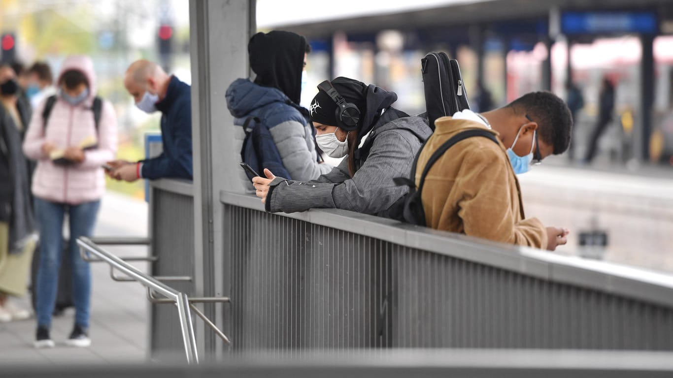 Maskenpflicht im oeffentlichen Personennahverkehr. Am Ostbahnhof warten Fahrgaeste auf ihren Zug,sie blicken auf ihre Sm