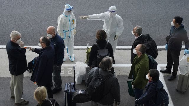 Arbeiter in Schutzkleidung sprechen mit Mitgliedern eines Teams der Weltgesundheitsorganisation (WHO) am Flughafen in Wuhan.