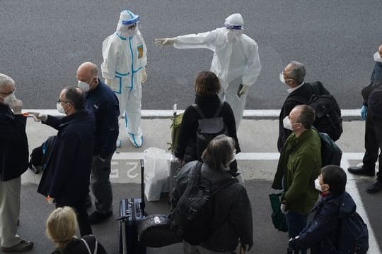 Arbeiter in Schutzkleidung sprechen mit Mitgliedern eines Teams der Weltgesundheitsorganisation (WHO) am Flughafen in Wuhan.