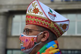 Ein Karnevalist trägt einen bunten Mundschutz bei der Sessionseröffnung am 11.11. in Köln: Die Traditionskorps hoffen nun auf die nächste Session.