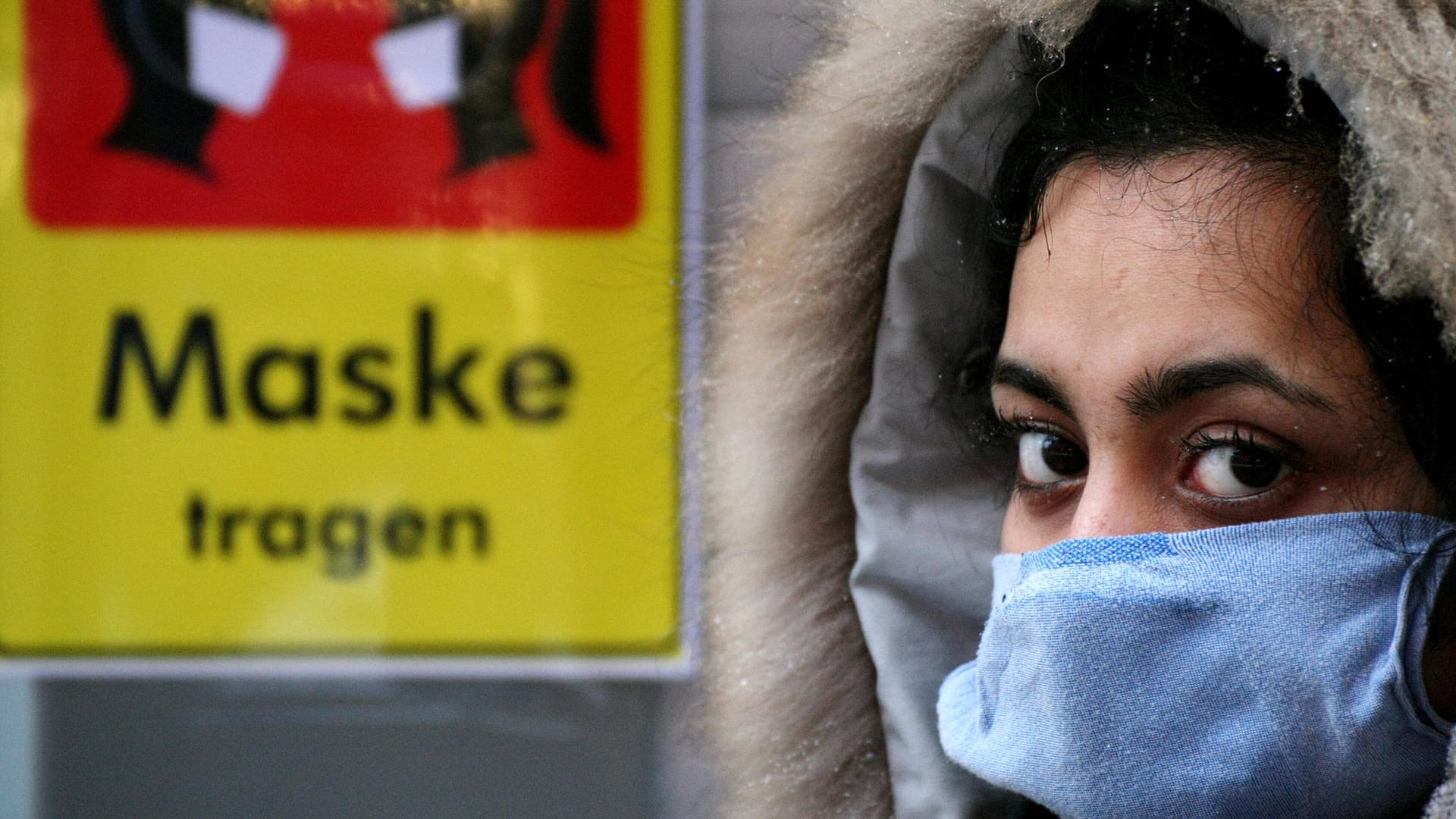 Eine Frau steht vor einem Schild, das Maskentragen fordert. Die aktuellen Corona-Zahlen scheinen sich zu stabilisieren.