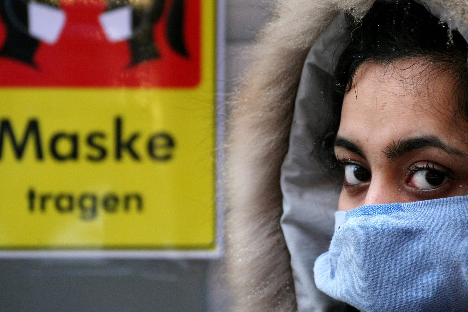 Eine Frau steht vor einem Schild, das Maskentragen fordert. Die aktuellen Corona-Zahlen scheinen sich zu stabilisieren.