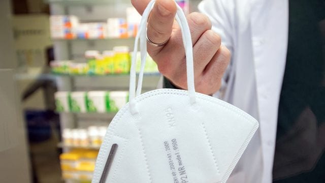 Ein Apotheker hält eine FFP2-Maske an einem Finger