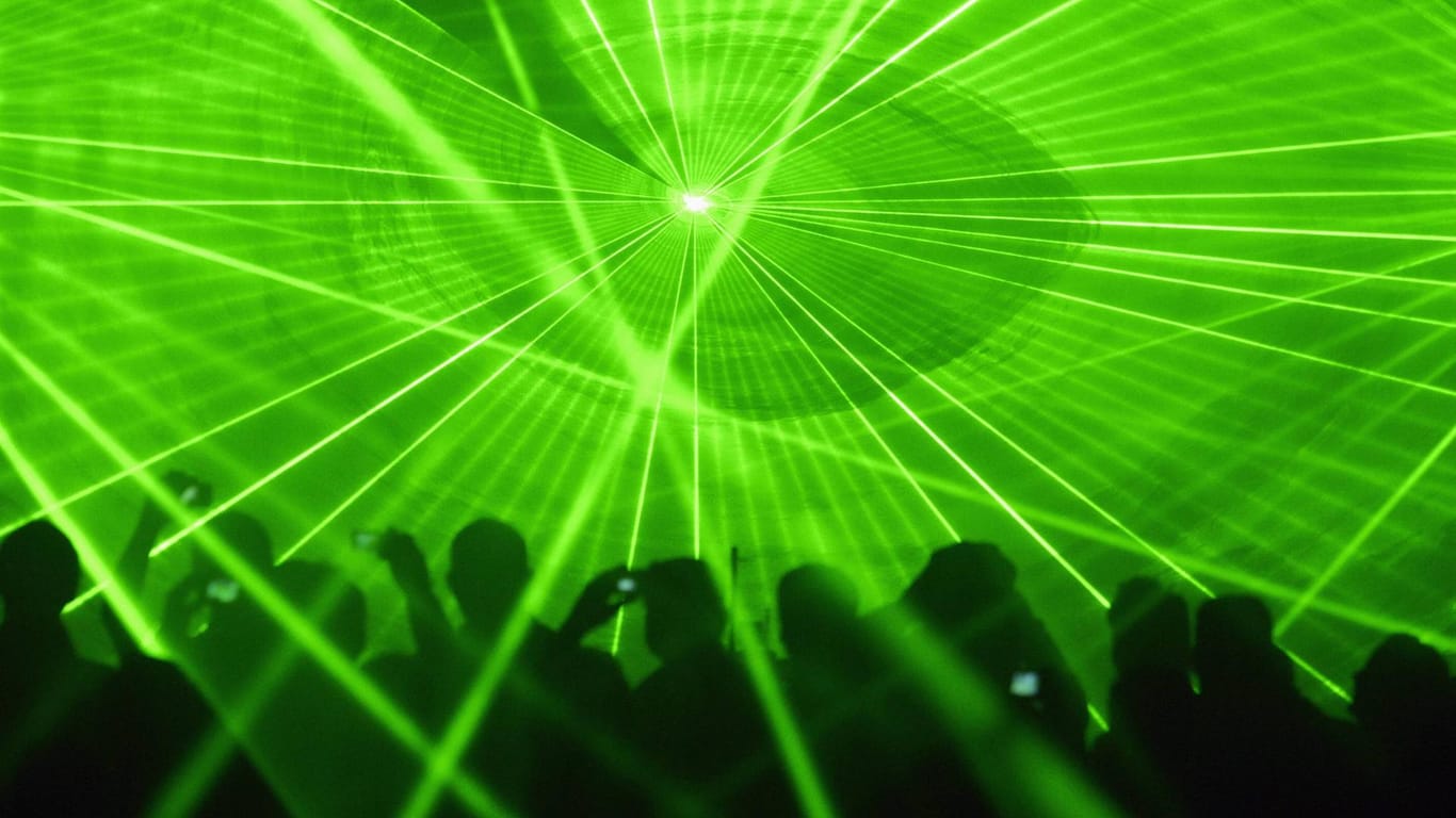 Grüne Laser leuchten auf einer Tanzfläche (Symbolbild): In Köln haben trotz der Corona-Beschränkungen Dutzende Raver in einem Wald gefeiert.