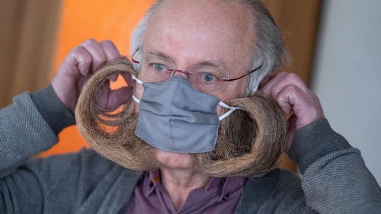 Jürgen Burkhardt, Bartträger und mehrfacher Bartweltmeister, demonstriert das Anlegen seines für ihn von einer Schneiderin angefertigten Mundschutzes.