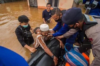 Rettungskräfte helfen einem älteren Mann in einem überfluteten Dorf in ihr Boot.