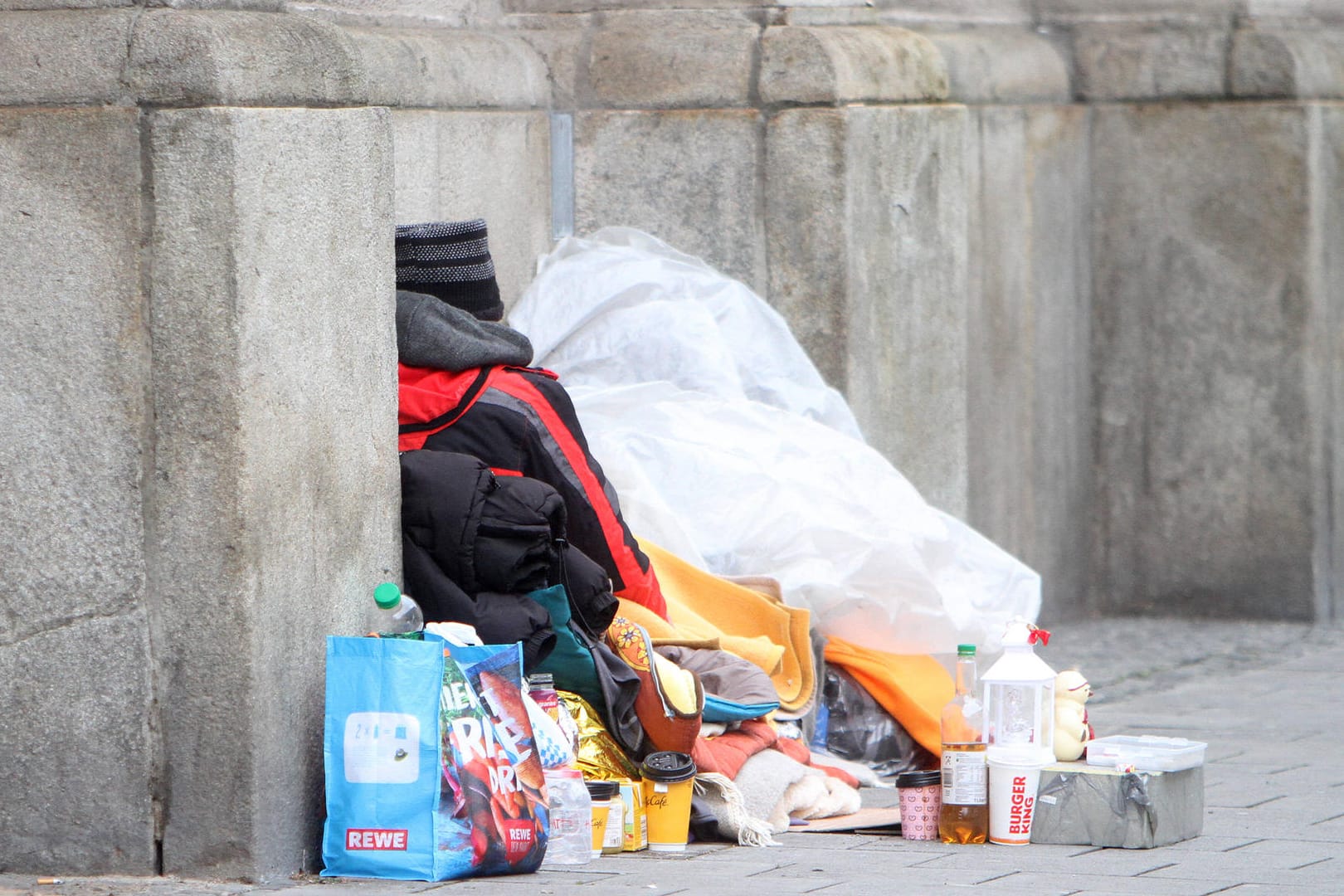 Obdachloser Mann liegt mit seinem Hab und Gut an einer Mauer (Symbolbild): In Mainz gab es in diesem Winter bisher drei Todesfälle von Wohnungslosen.